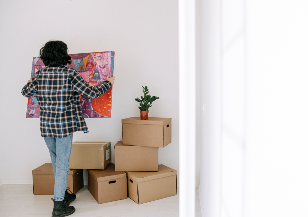 woman surrounded by moving boxes is taking down a painting from a wall