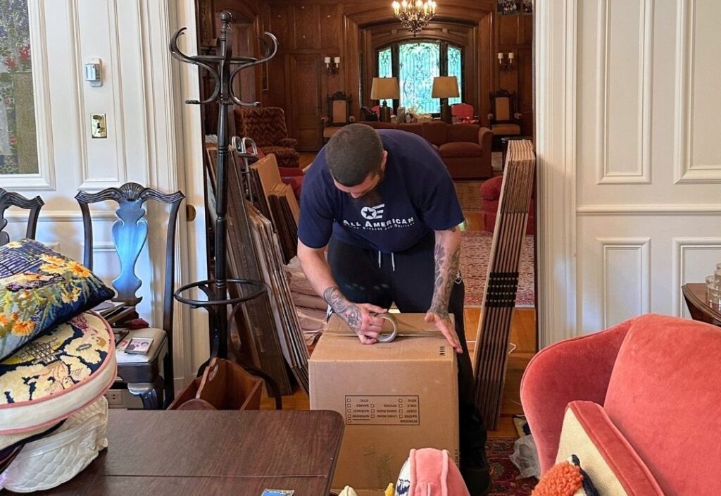 mover carefully packing and sealing a cardboard box filled with fragile items during a residential move